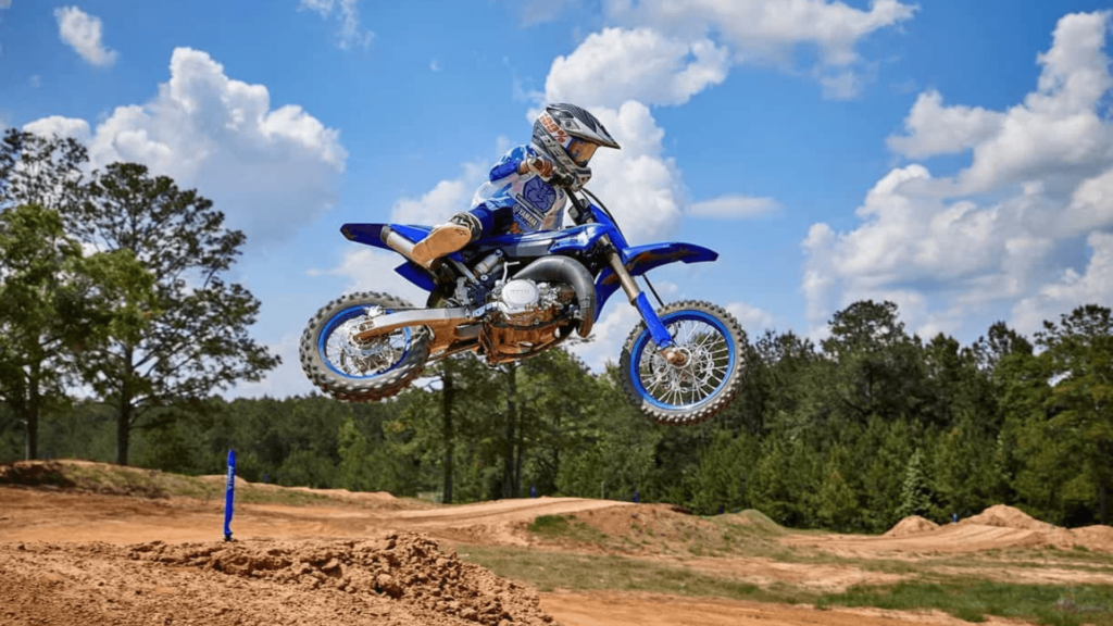 Yamaha YZ65 2026 azul com branca saltando de lado em uma pista de motocross.