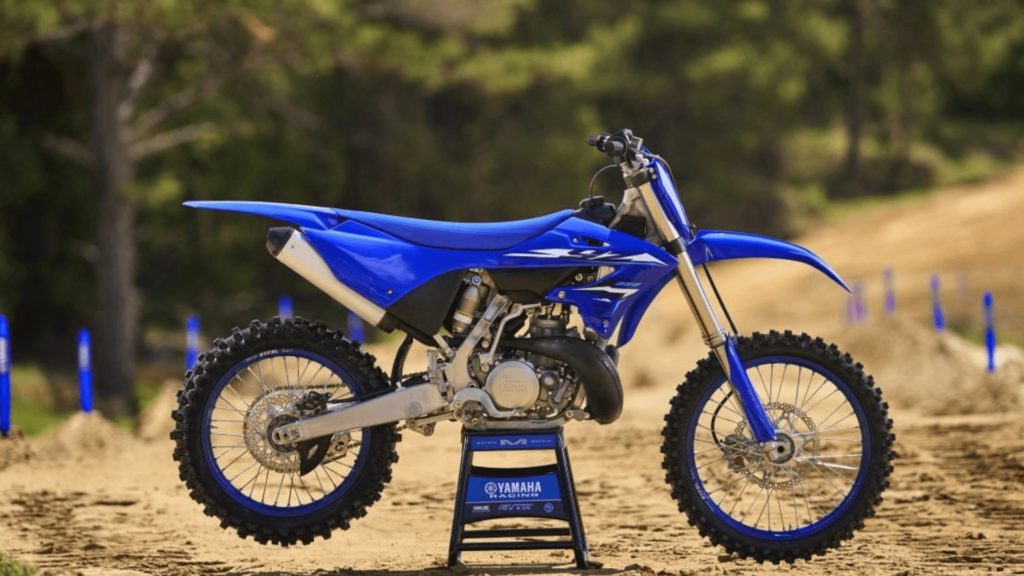 Lateral da Yamaha YZ250 2026 azul com branca parada em cima de um cavalete no meio da pista.