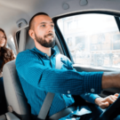 Homem que trabalha na Uber de azul com uma passageira no banco de trás.