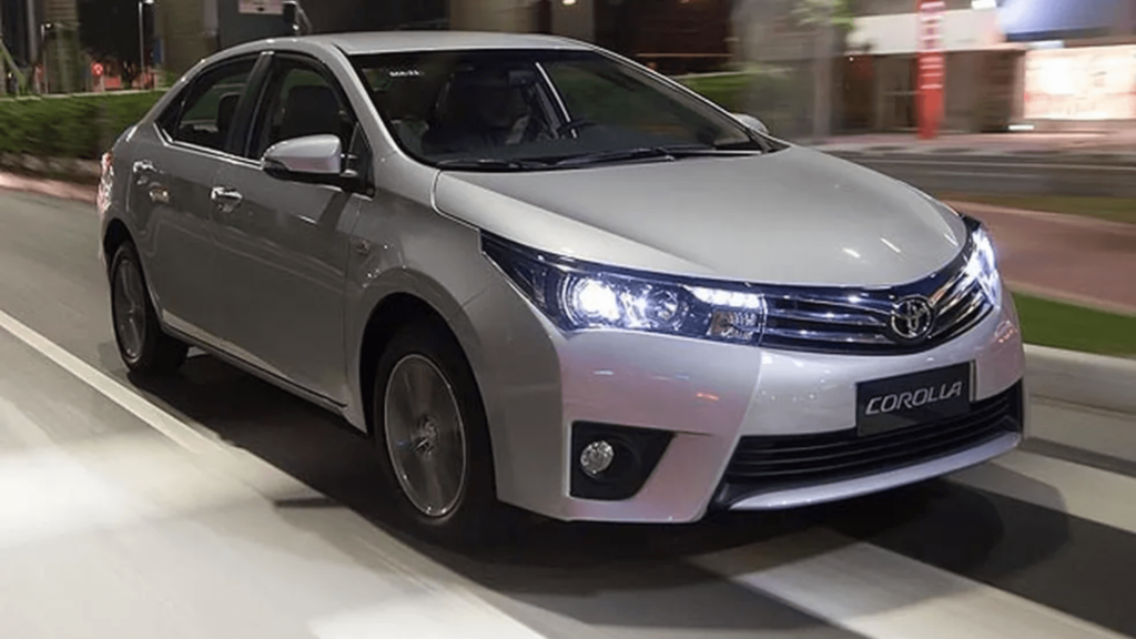 Toyota Corolla prata com os faróis acesos na estrada.