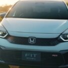 Frente do Honda Fit branco com os faróis acesos.