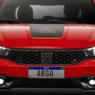 Frente do Fiat Argo Trekking vermelho com os faróis acesos no fundo branco.