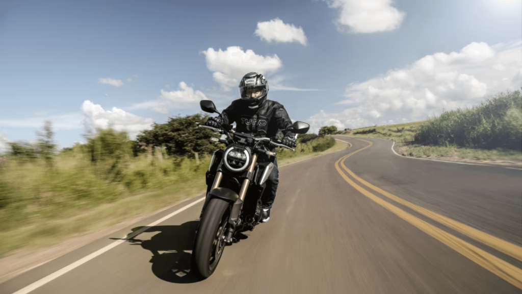 Homem de preto em cima de uma moto em velocidade na estrada de asfalto de dia.