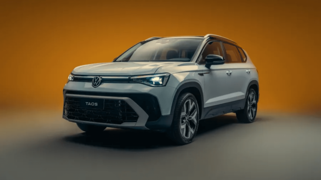 Volkswagen Taos 2026 cinza parado na diagonal em um fundo laranja.