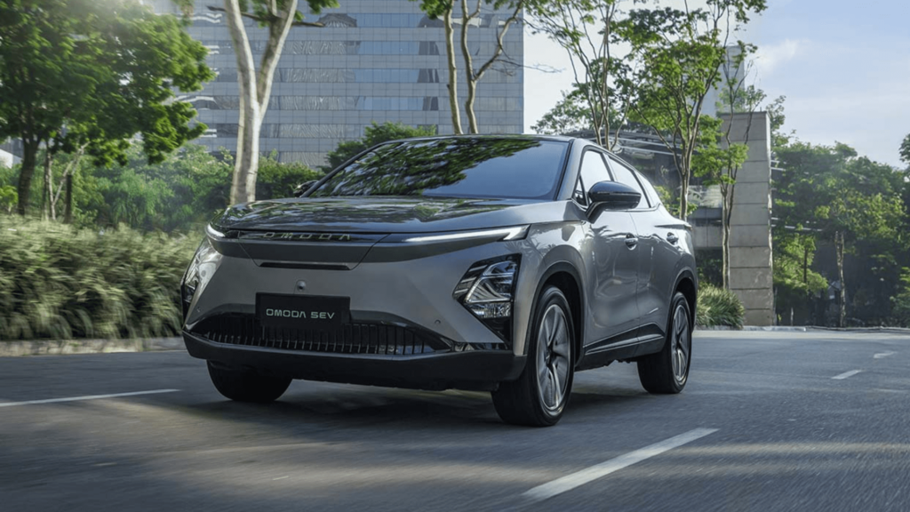Novo Omoda 5 HEV cinza em movimento na estrada com os faróis acesos.