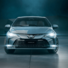 Toyota Corolla azul parado de frente com os faróis acesos.