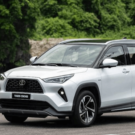 Toyota Yaris Cross branco parado na diagonal em cima de um asfalto com um lago no fundo.