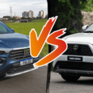 Toyota Yaris Cross branco parado na diagonal e do outro lado da foto está o Fiat Pulse Audace Hybrid azul na estrada.