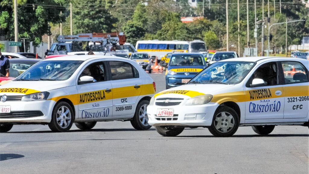 Dois carros da autoescola branco parados na diagonal.
