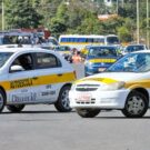 Dois carros da autoescola branco parados na diagonal.