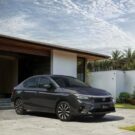 Honda City cinza parado na frente de uma garagem.