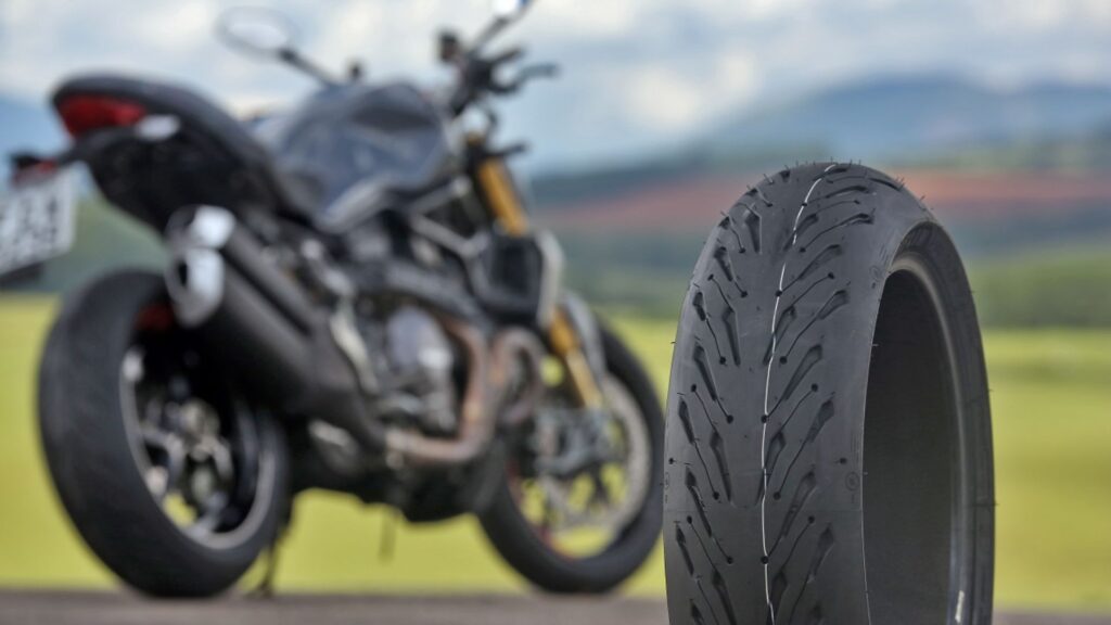 Pneu de uma moto com uma moto no fundo parada.